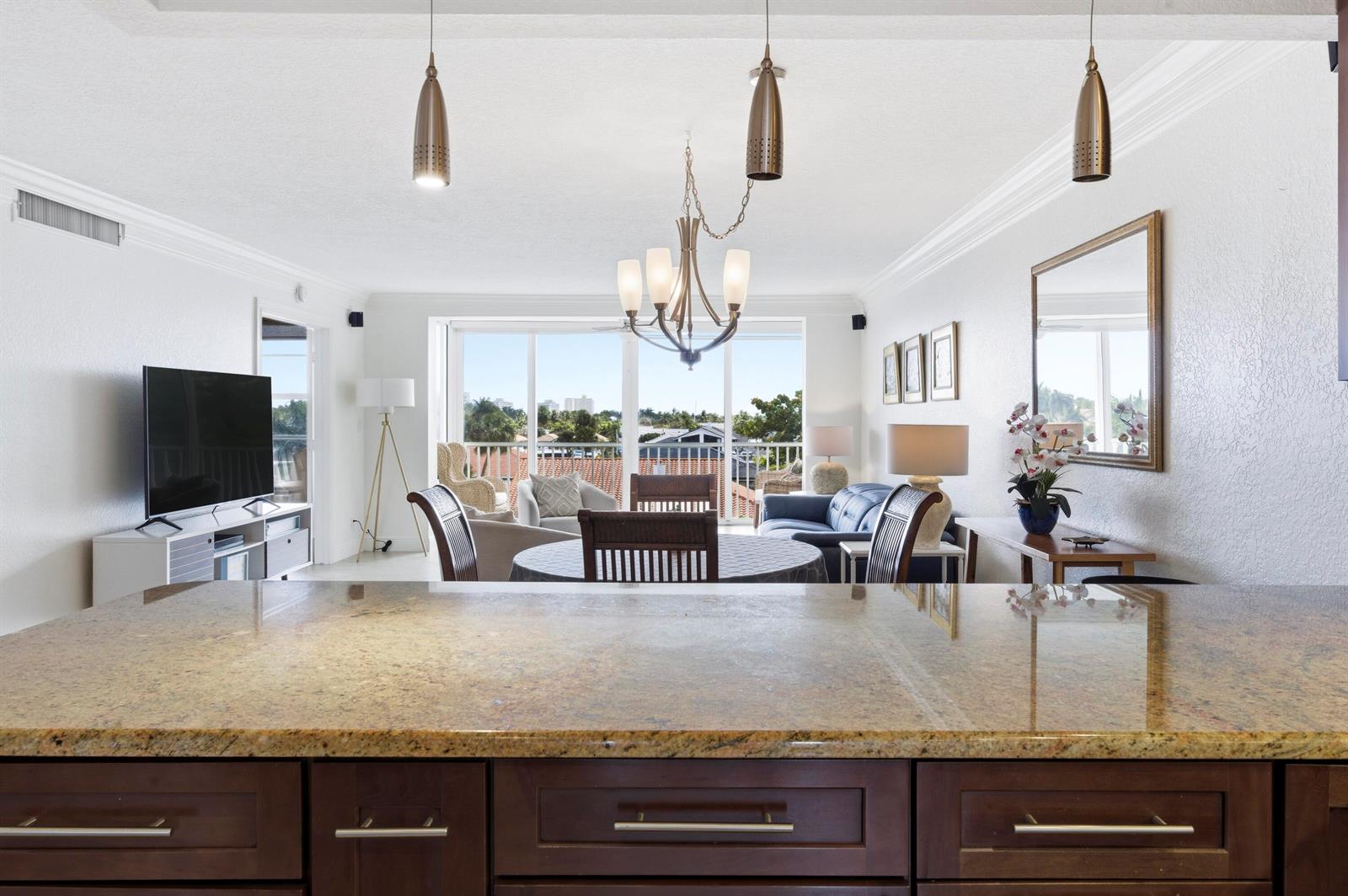 A kitchen island with granite countertops overlooks a dining area and living room with balcony — 3000 NE 48th Court # 406, Lighthouse Point FL 33064, LIGHTHOUSE POINT, FL
