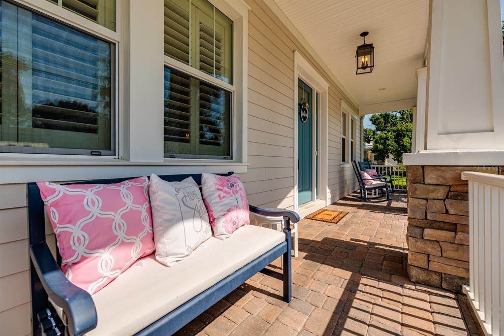 A covered front porch features a blue bench with pink pillows and stone pillar accents — 852 CORDOVA BOULEVARD NE, ST PETERSBURG, FL