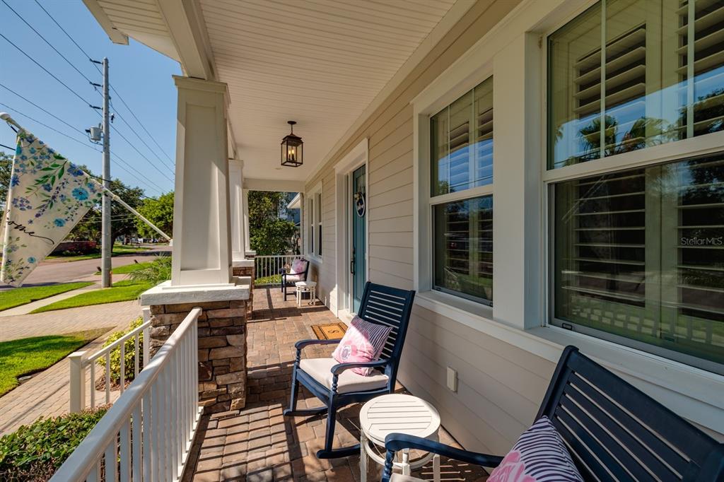A covered front porch features stone-based columns, a brick floor, and blue rocking chairs — 852 CORDOVA BOULEVARD NE, ST PETERSBURG, FL