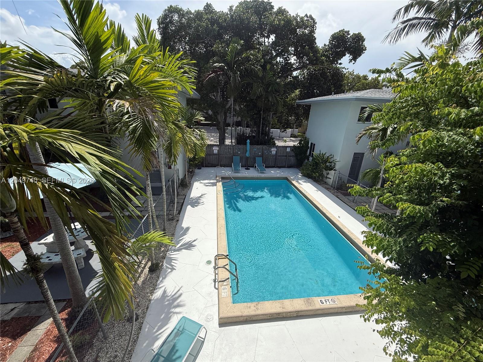 An outdoor swimming pool is situated between two buildings surrounded by palm trees and foliage — 7441 SW 59th Pl # 28, South Miami FL 33143, SOUTH MIAMI, FL