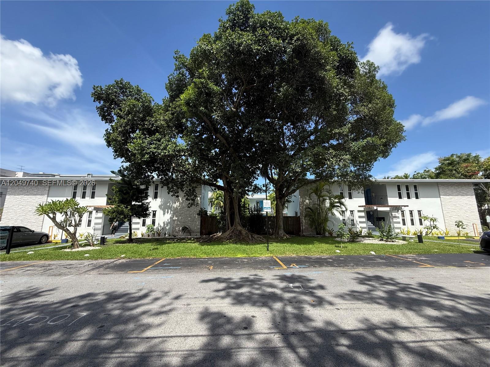 A large tree stands between two white apartment buildings with a parking lot in front — 7441 SW 59th Pl # 28, South Miami FL 33143, SOUTH MIAMI, FL