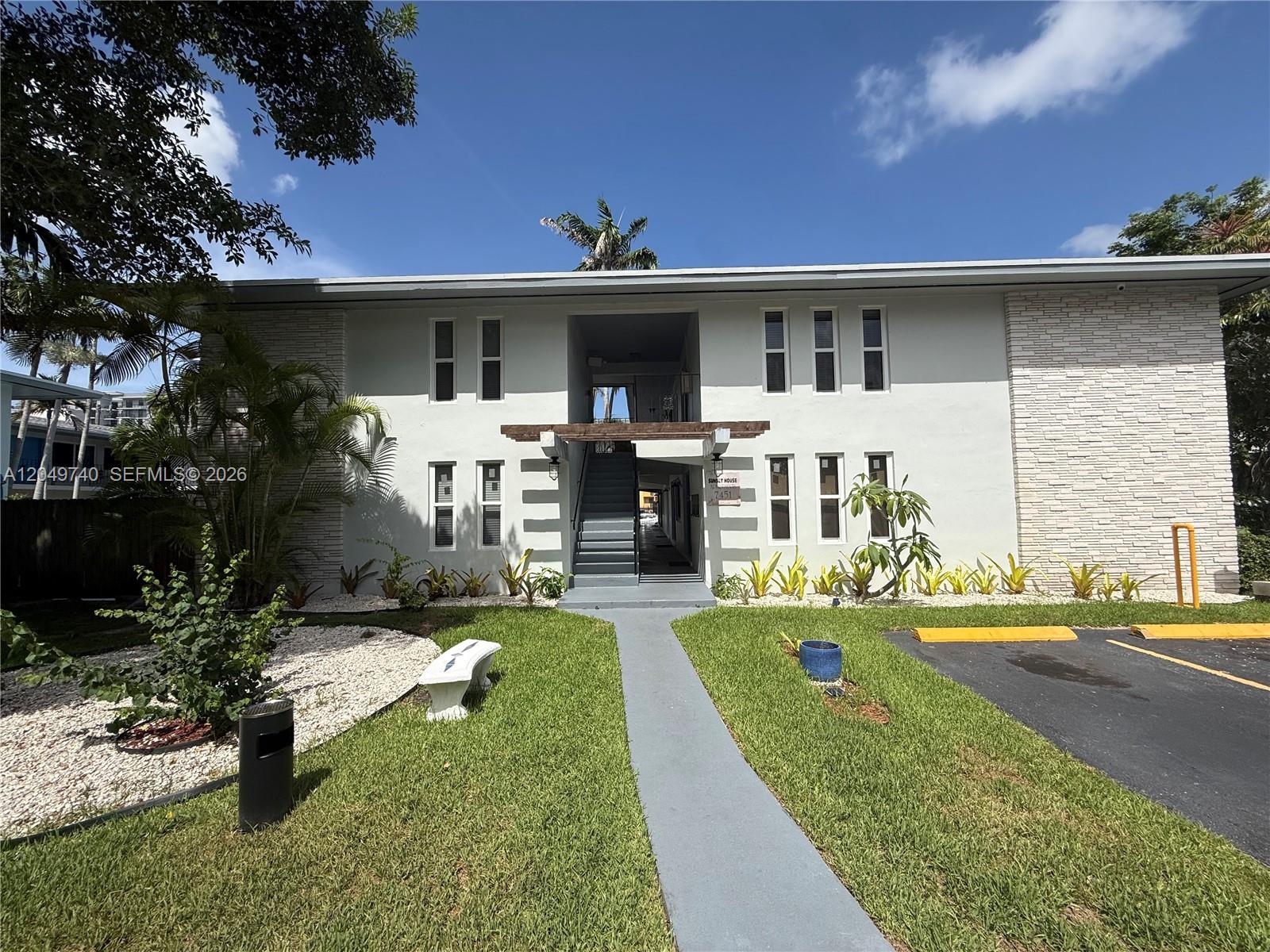 A two-story apartment building features a central staircase, white stone accents, and a landscaped lawn — 7441 SW 59th Pl # 28, South Miami FL 33143, SOUTH MIAMI, FL