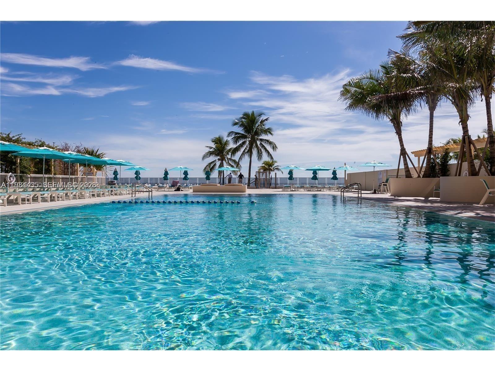 A swimming pool with lounge chairs and umbrellas under a blue sky with palm trees — 2501 S Ocean Dr # 429, Hollywood FL 33019, HOLLYWOOD, FL