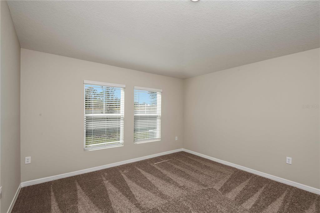 An empty bedroom features beige walls, brown carpet, and two windows with white blinds — 1362 PALMEROY ROAD, HAINES CITY, FL