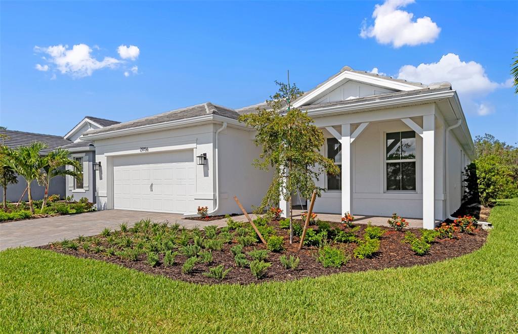A white single-story house with a two-car garage and a front porch under a blue sky — 26724 SANDY BREEZE DRIVE, ENGLEWOOD, FL