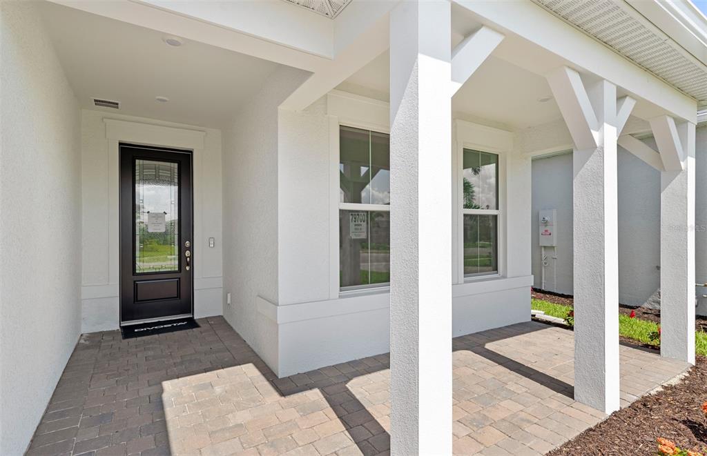 A covered front porch with white columns, a black front door, and paver flooring — 26724 SANDY BREEZE DRIVE, ENGLEWOOD, FL