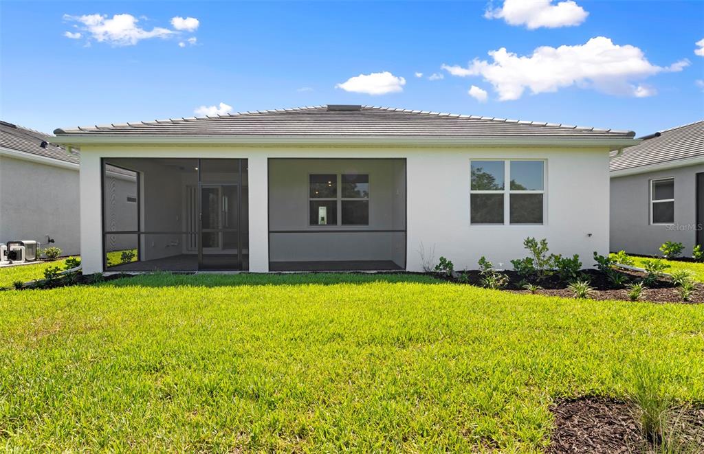 The back exterior of a single-story house features a screened-in lanai and a grassy yard — 26724 SANDY BREEZE DRIVE, ENGLEWOOD, FL