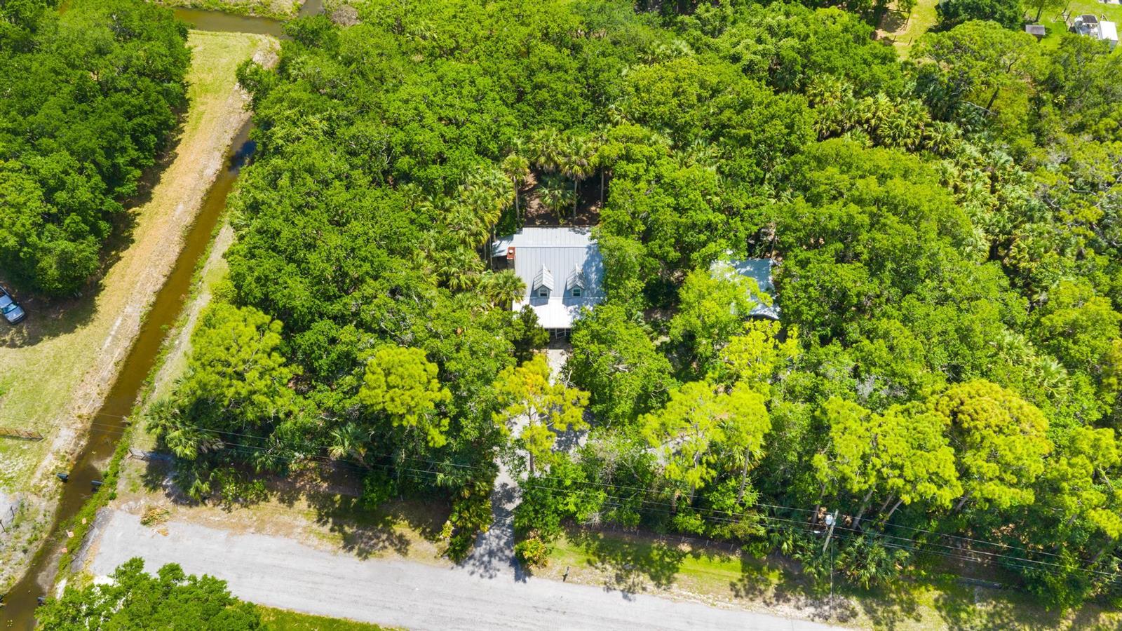 An aerial view shows a house with a metal roof nestled within a dense forest — 15740 N 99th St Street N, FL 33412, FL