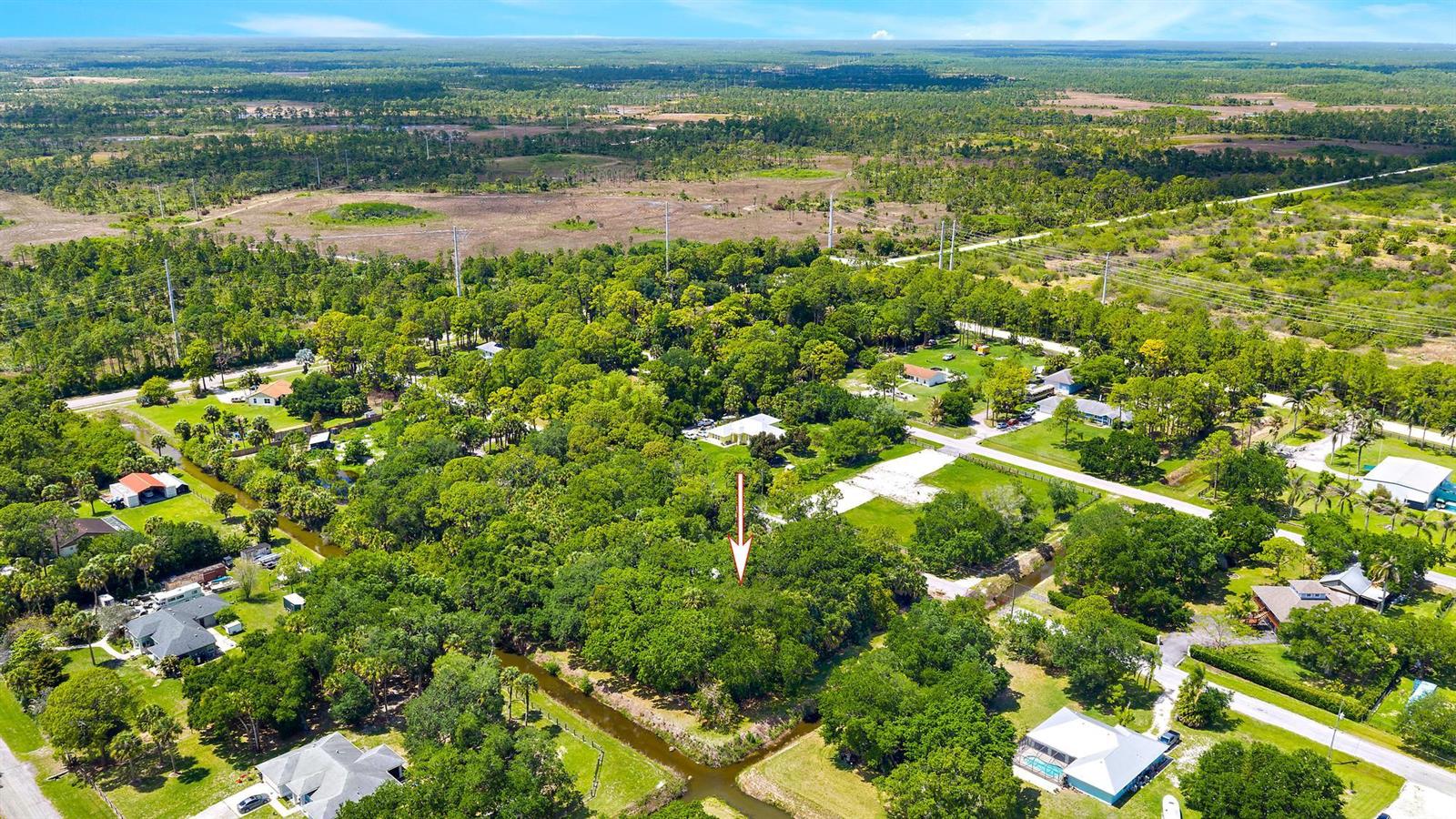 An aerial view shows a wooded residential lot marked by an arrow amidst surrounding homes — 15740 N 99th St Street N, FL 33412, FL