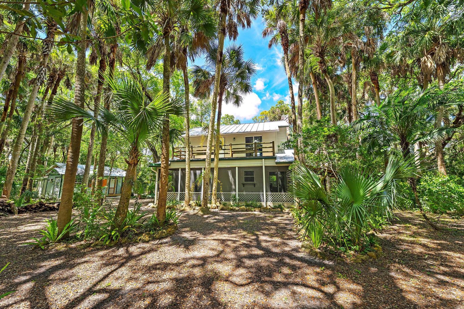 A two-story house with a screened porch and balcony sits in a wooded, palm-filled lot — 15740 N 99th St Street N, FL 33412, FL