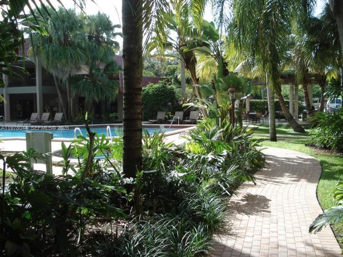 A paved walkway leads past lush tropical landscaping toward a swimming pool and building exterior — 9301 SW 92nd Ave # 207C, Miami FL 33176, MIAMI, FL
