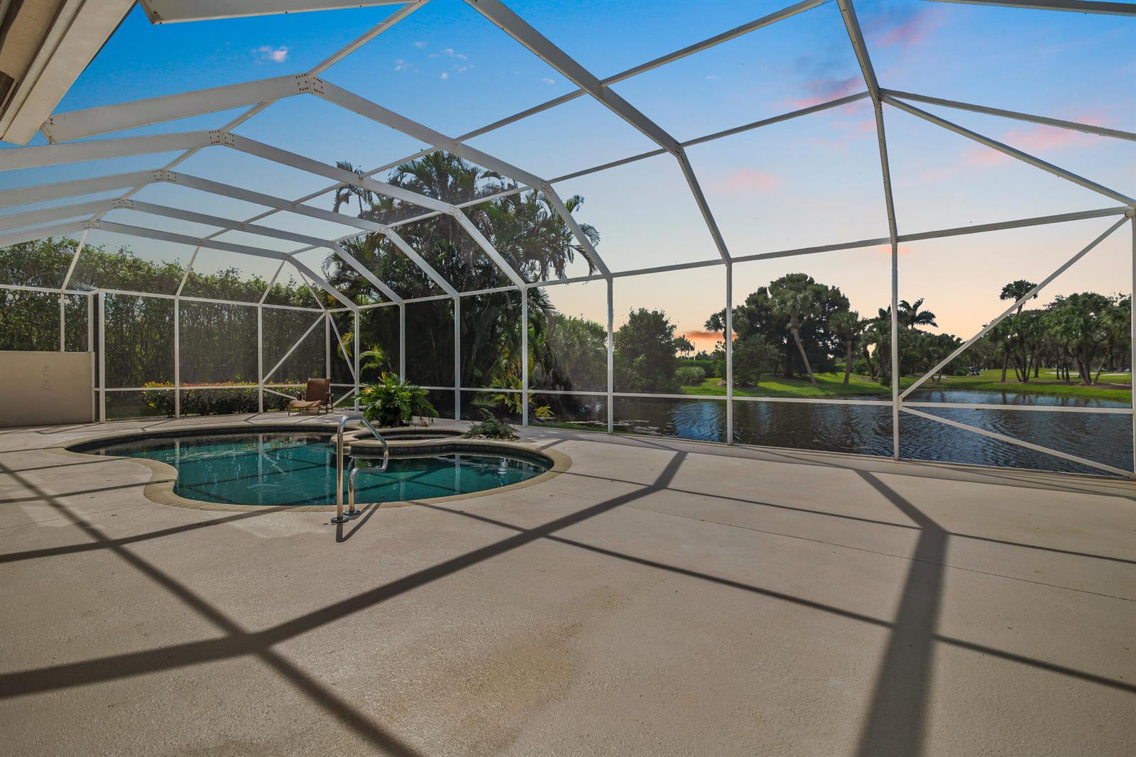 A screened-in pool patio overlooks a lake and golf course at sunset — 9741 Spray Drive, West Palm Beach FL 33411, WEST PALM BEACH, FL