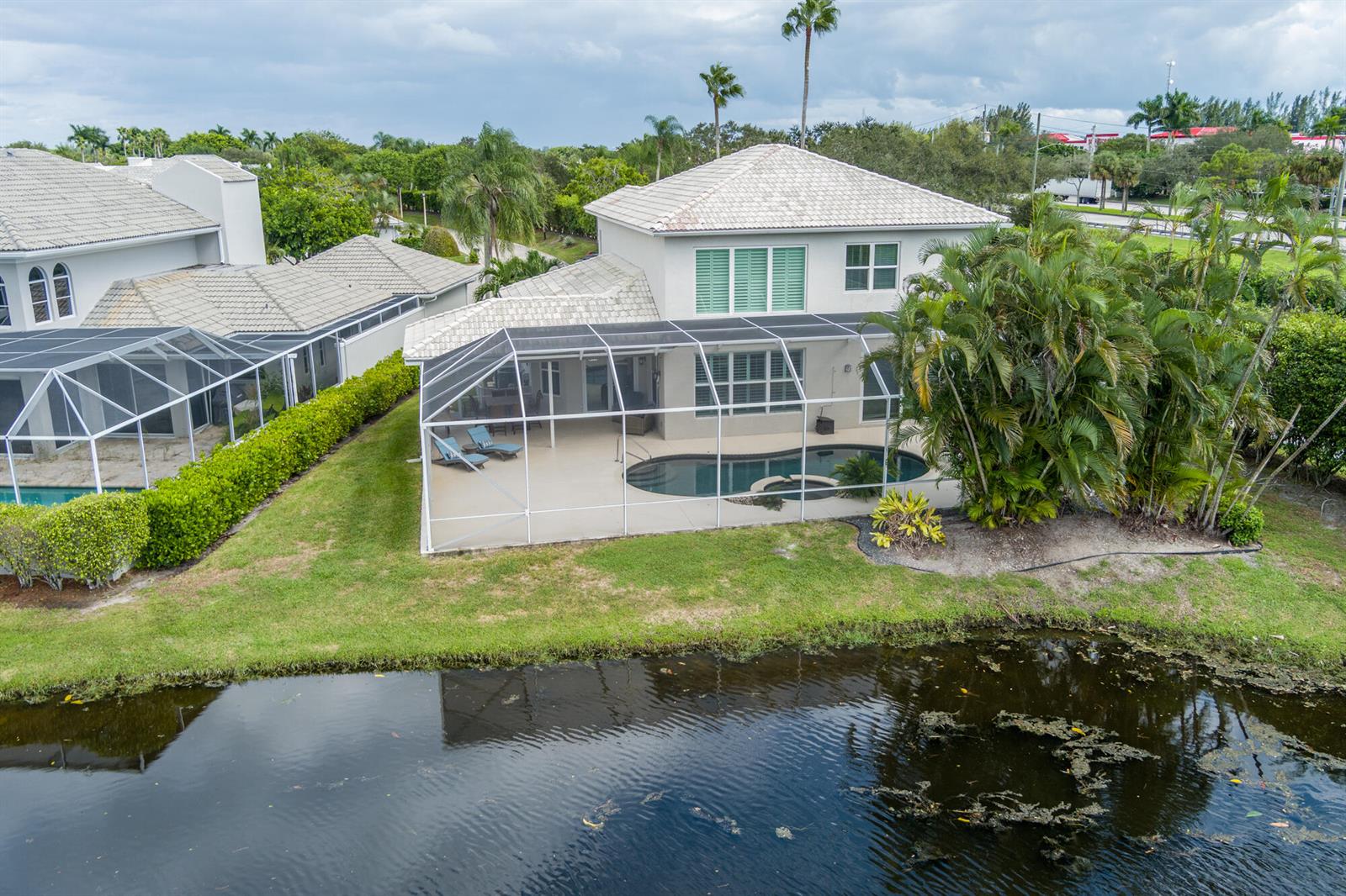 An aerial view of a two-story house with a screened pool enclosure and a pond — 9741 Spray Drive, West Palm Beach FL 33411, WEST PALM BEACH, FL