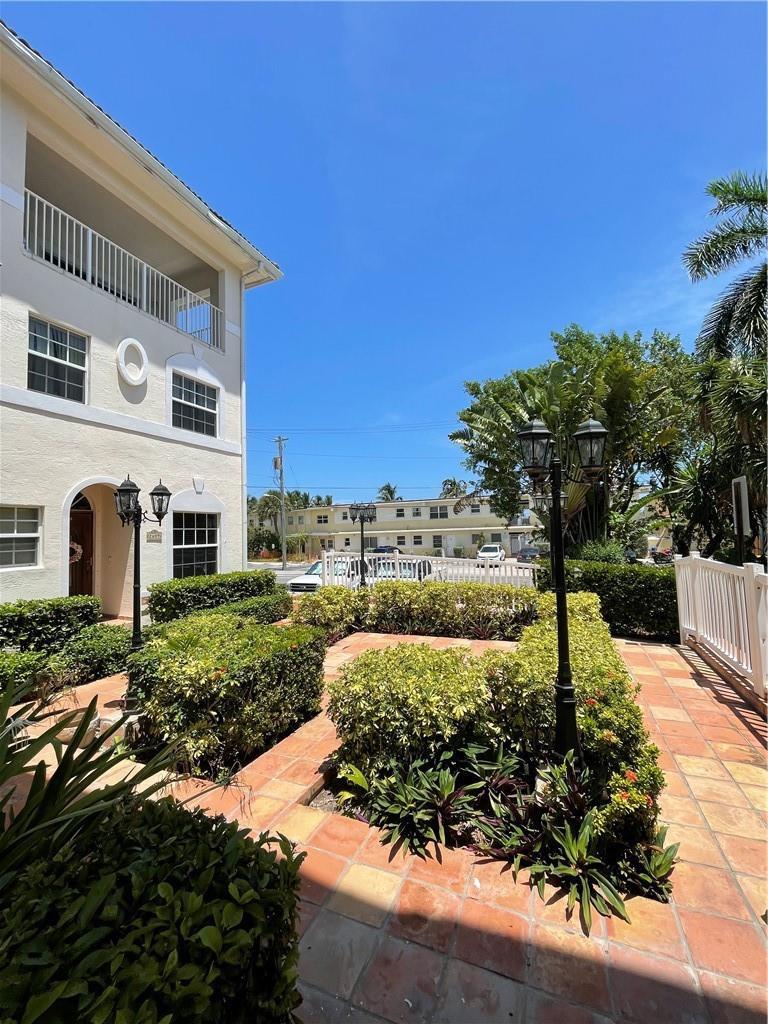 A view of a tiled courtyard with manicured hedges and a multi-story apartment building — 2605 Bay Drive, Pompano Beach FL 33062, POMPANO BEACH, FL