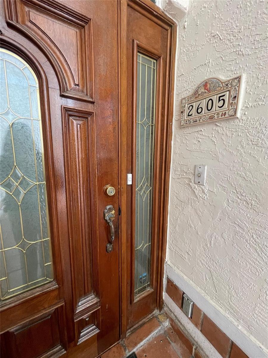 A wooden front door with glass panels sits next to a house number plaque — 2605 Bay Drive, Pompano Beach FL 33062, POMPANO BEACH, FL