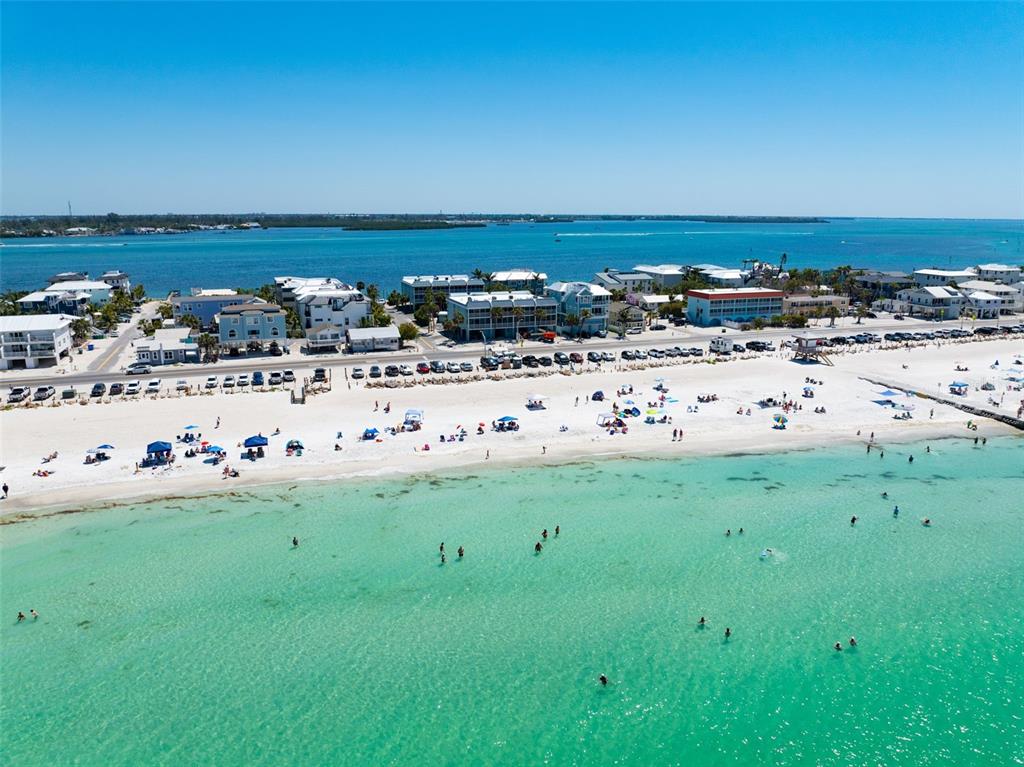 An aerial view shows a sandy beach with people, parked cars, and coastal buildings — 901 GULF DRIVE S UNIT 14, BRADENTON BEACH, FL