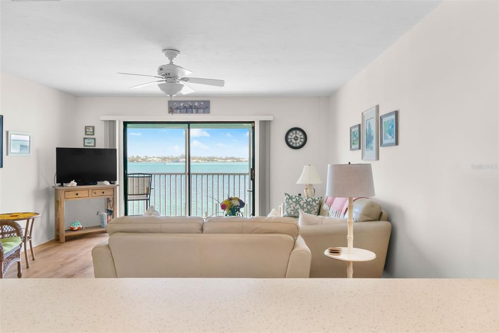 A living room features a beige sofa, television, ceiling fan, and a balcony overlooking water — 901 GULF DRIVE S UNIT 14, BRADENTON BEACH, FL