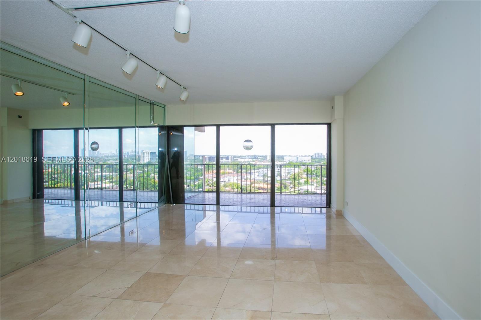 An empty room features beige tile floors, a mirrored wall, track lighting, and a balcony — 1800 NE 114th St # 1502, Miami FL 33181, MIAMI, FL