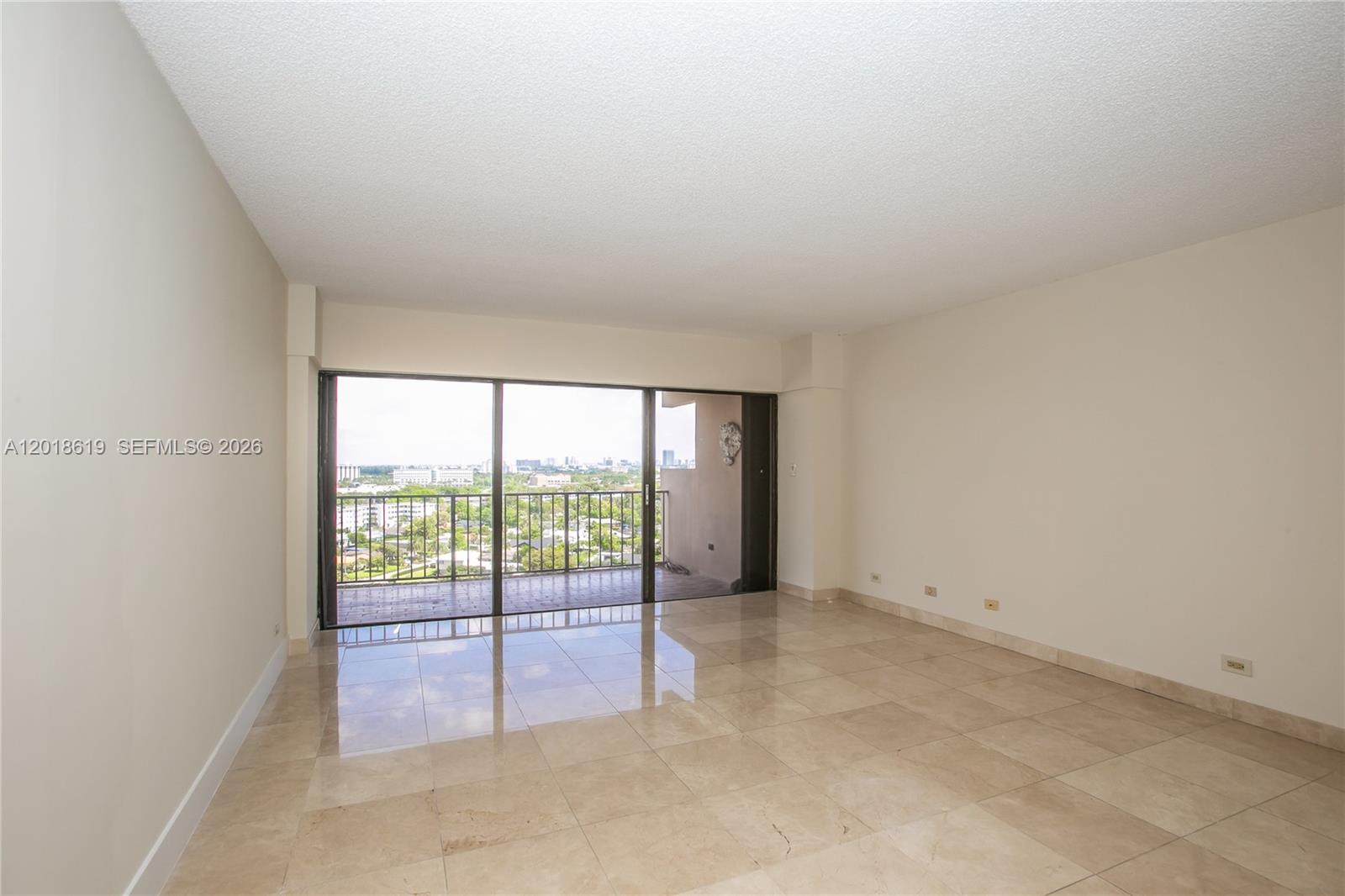An empty room features beige tile flooring, white walls, and a sliding glass door to a balcony — 1800 NE 114th St # 1502, Miami FL 33181, MIAMI, FL