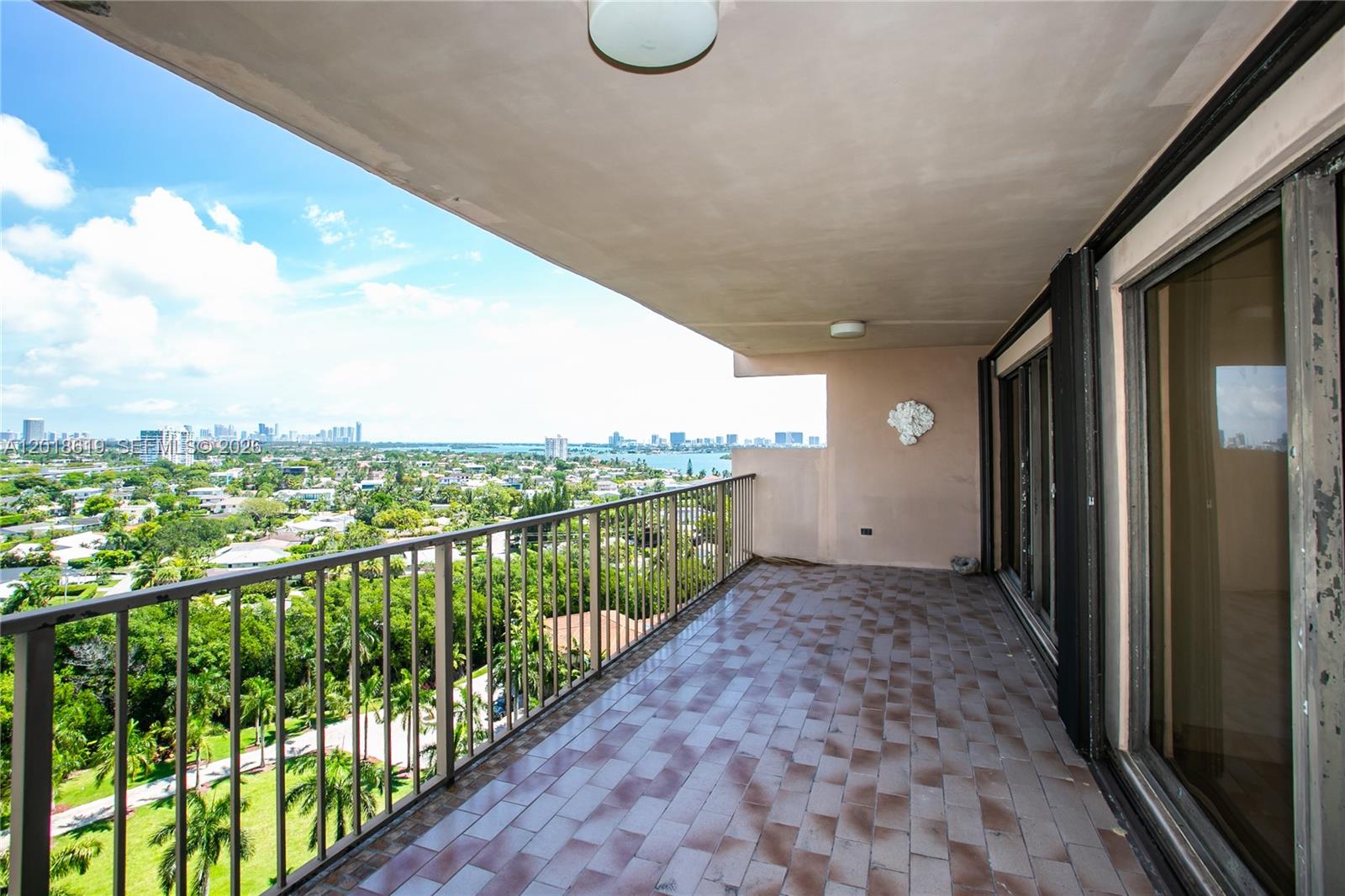 A covered balcony with tiled flooring overlooks a suburban landscape and a distant city skyline — 1800 NE 114th St # 1502, Miami FL 33181, MIAMI, FL
