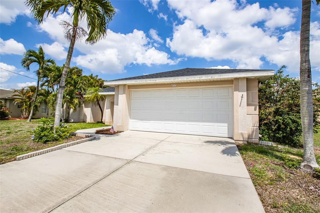 A single-story house with a white garage door, concrete driveway, and surrounding palm trees — 5333 SW 16TH PLACE, CAPE CORAL, FL
