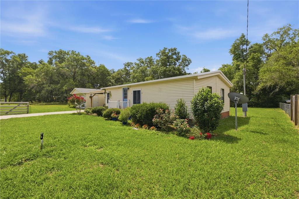A single-story beige mobile home sits on a grassy lot with mature trees nearby — 11140 SW 109TH PLACE, DUNNELLON, FL