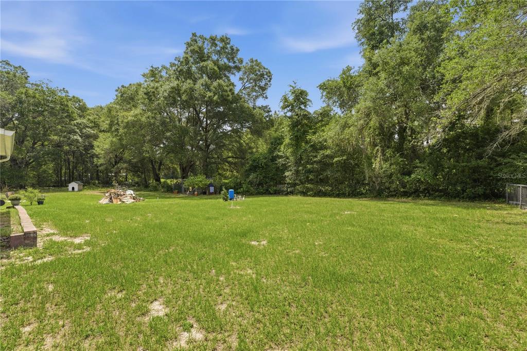 A large, grassy backyard features mature trees and a small shed in the distance — 11140 SW 109TH PLACE, DUNNELLON, FL