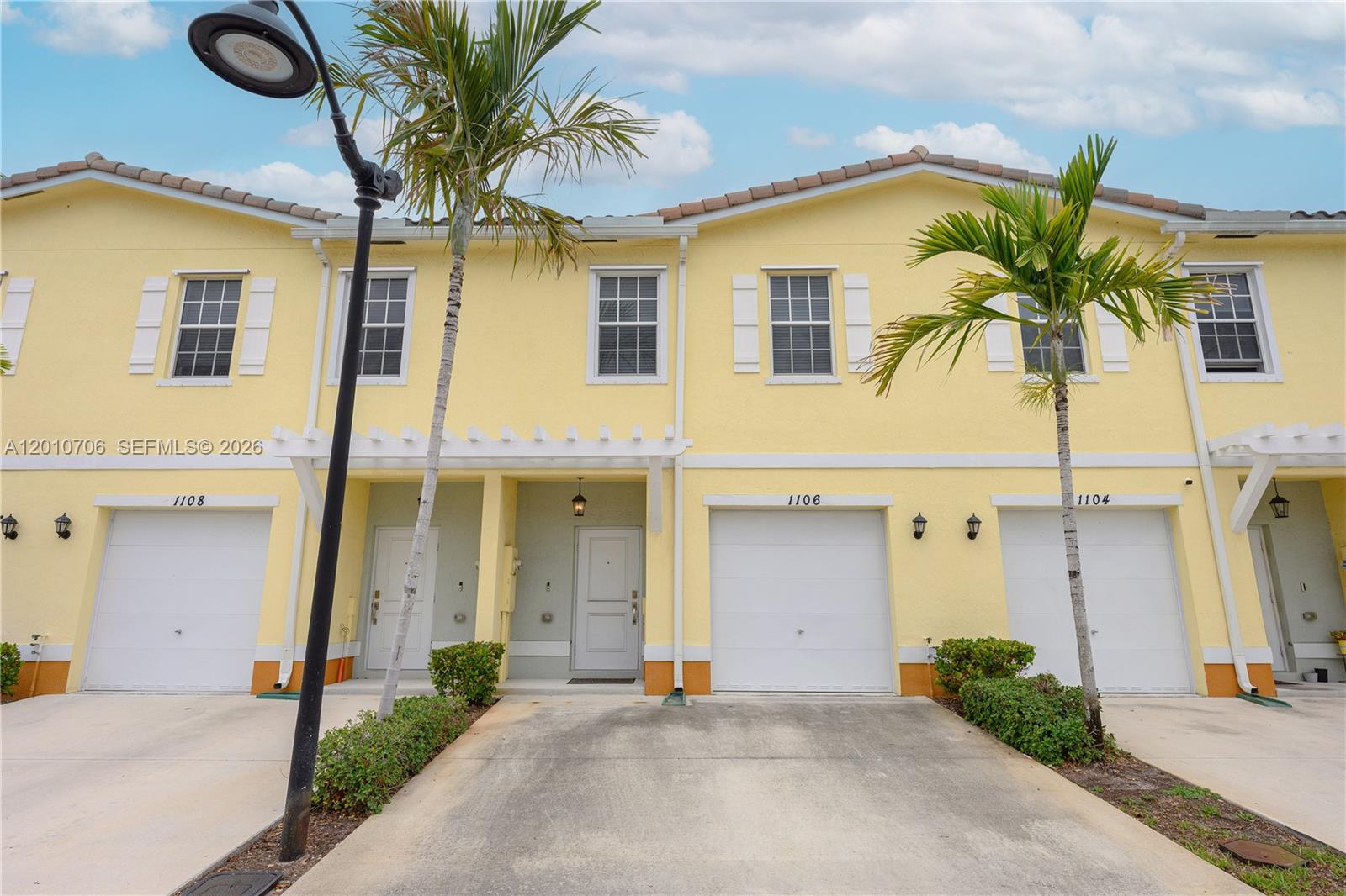 A row of yellow two-story townhouses with white garage doors and palm trees in front — 1106 NW 40th Ter, Lauderhill FL 33313, LAUDERHILL, FL