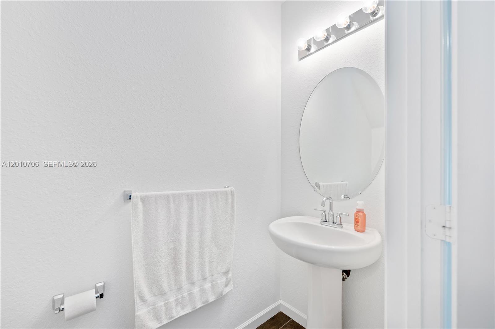A small bathroom features a white pedestal sink, a round mirror, and a towel rack — 1106 NW 40th Ter, Lauderhill FL 33313, LAUDERHILL, FL