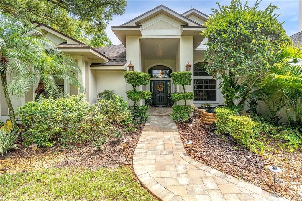 A paved walkway leads to the front entrance of a single-story house with landscaped gardens — 5328 MACOSO COURT, NEW PORT RICHEY, FL