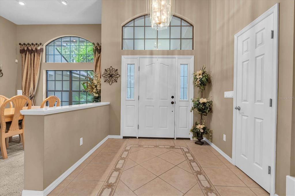 A tiled entryway features a white front door with sidelights, a transom window, and chandelier — 5328 MACOSO COURT, NEW PORT RICHEY, FL