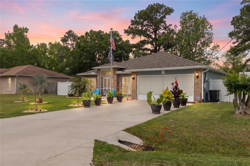 A single-story house with a two-car garage, a concrete driveway, and potted plants at sunset — 7 RANBAY PLACE, PALM COAST, FL