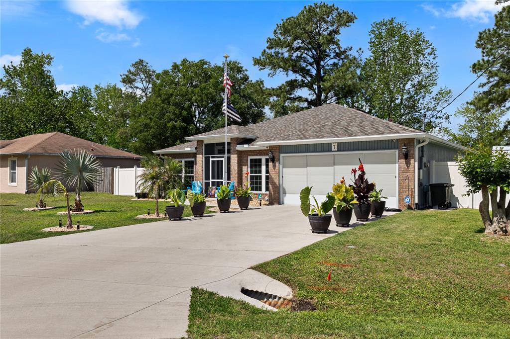A single-story brick house with a concrete driveway, potted plants, and a flag pole — 7 RANBAY PLACE, PALM COAST, FL