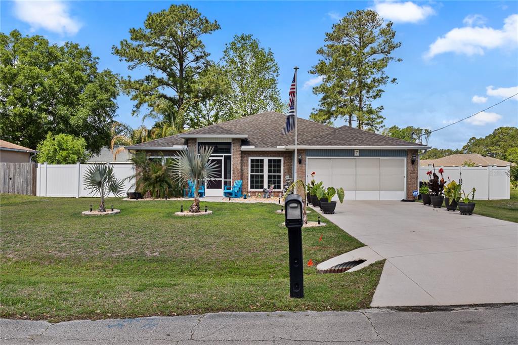 A single-story brick house with a two-car garage, white vinyl fencing, and a front lawn — 7 RANBAY PLACE, PALM COAST, FL