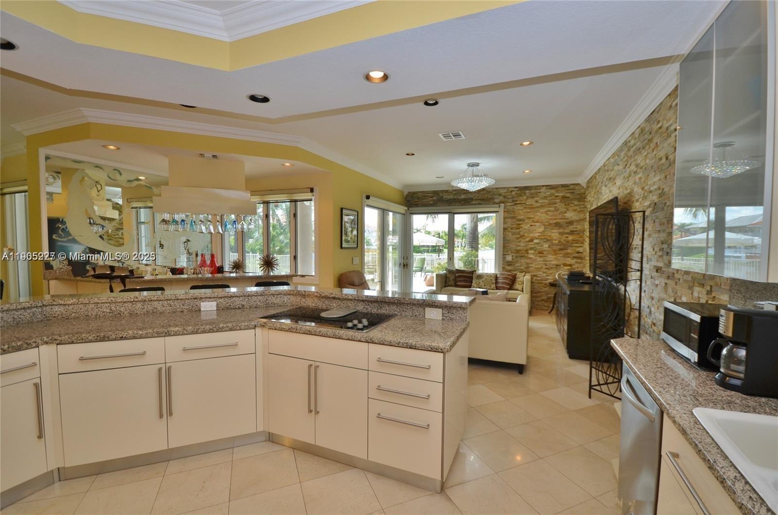 A kitchen with granite countertops and white cabinets overlooks a living area with stone walls — 16232 NW 79th Ave, Miami Lakes FL 33016, MIAMI LAKES, FL