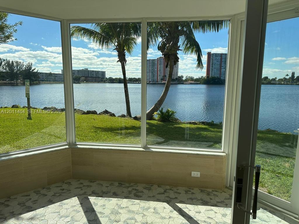 A sunroom with tiled flooring and large windows overlooking a lake and palm trees — 1302 NE 191st St # A114, Miami FL 33179, MIAMI, FL
