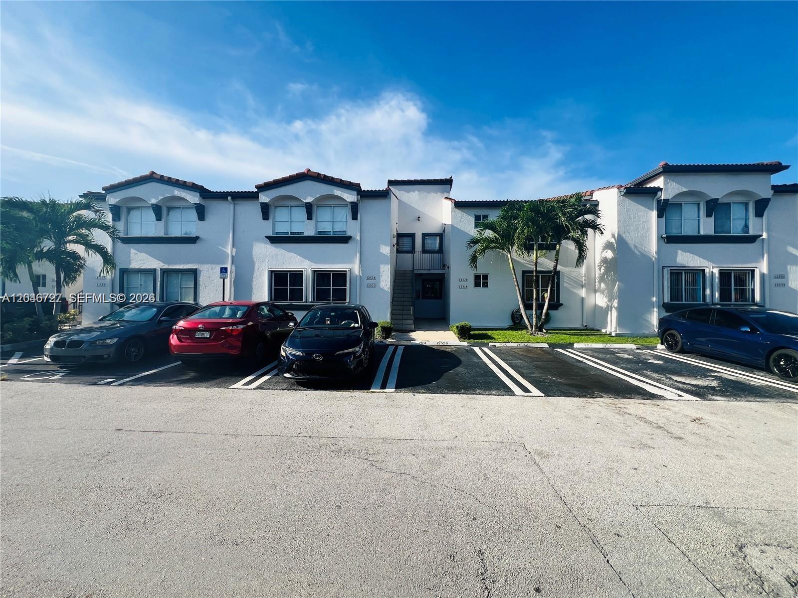 A two-story white stucco apartment building features a central staircase and a paved parking lot — 12526 NW 11th Trl # 207, Miami FL 33182, MIAMI, FL