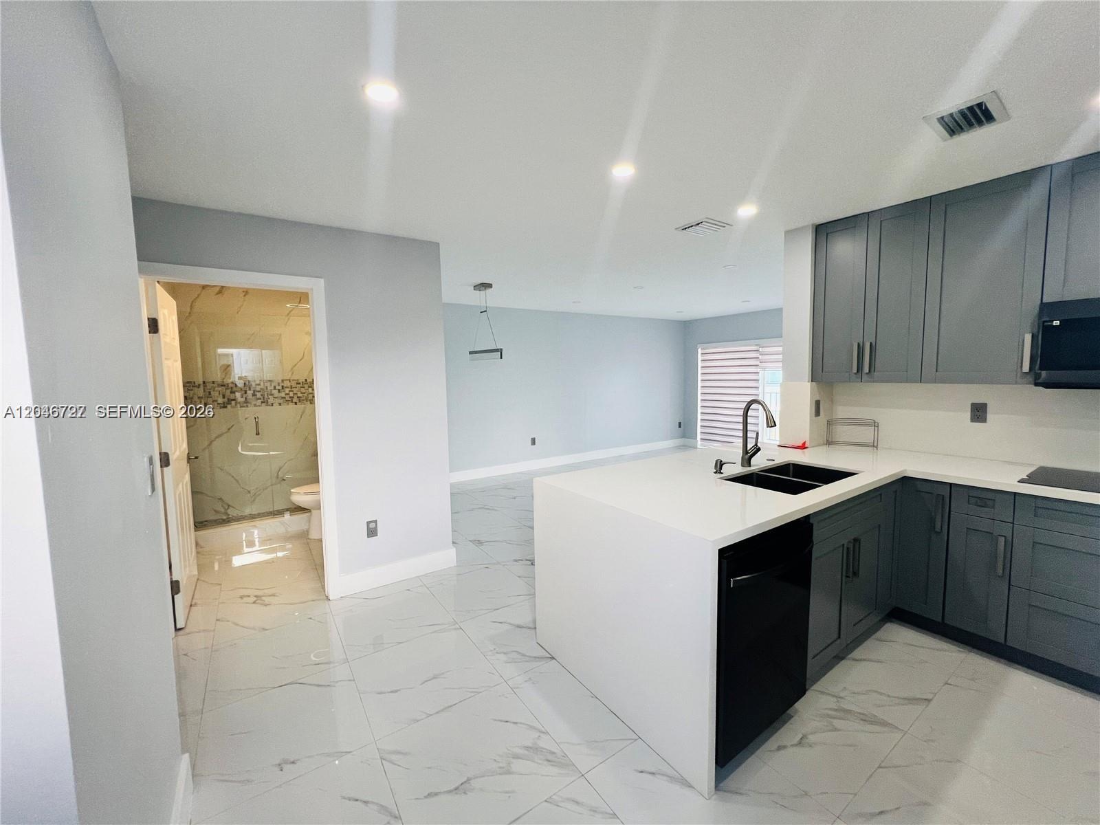 A modern kitchen with gray cabinets and a white island overlooks an open living area — 12526 NW 11th Trl # 207, Miami FL 33182, MIAMI, FL