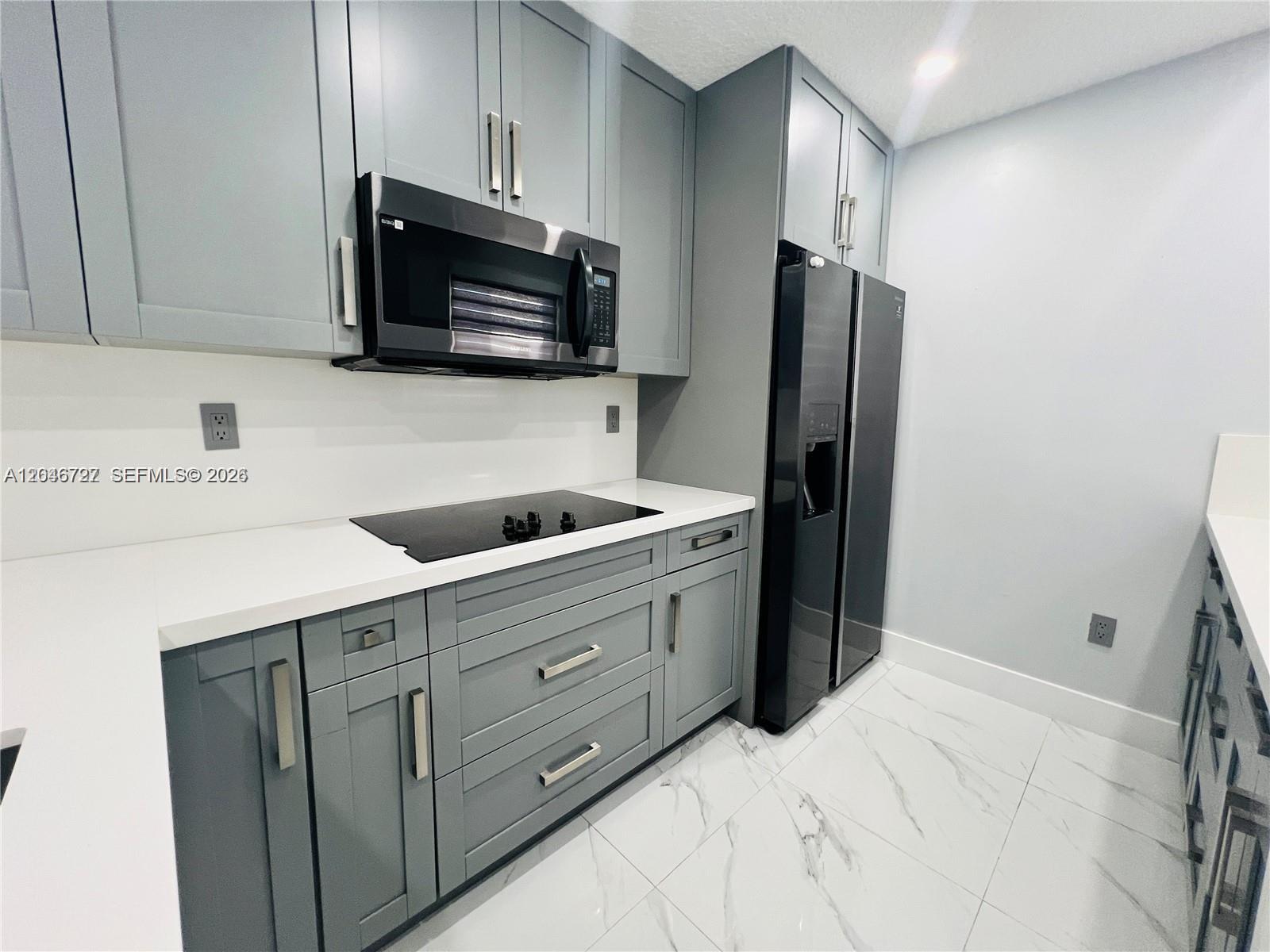 A modern kitchen features gray cabinets, black appliances, white countertops, and white marble-patterned tile flooring — 12526 NW 11th Trl # 207, Miami FL 33182, MIAMI, FL