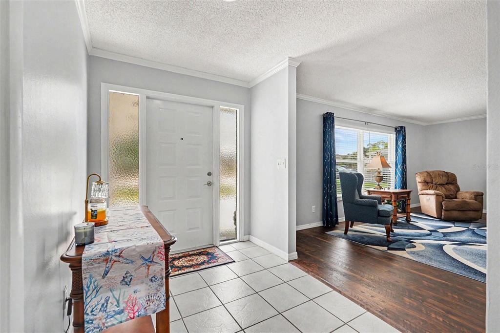A tiled entryway leads into a living room with hardwood floors and a blue rug — 1501 NEW BEDFORD DRIVE, SUN CITY CENTER, FL