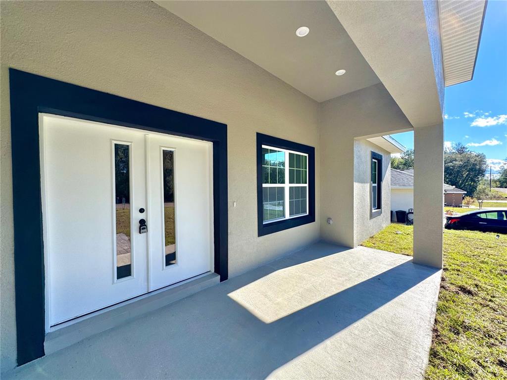 A covered concrete porch features a white double front door and a window with dark trim — 8191 N PICKINZ WAY, CITRUS SPRINGS, FL