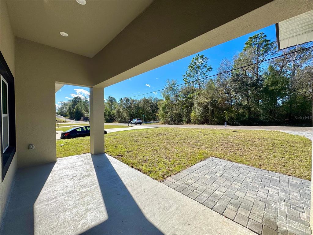 A covered concrete patio overlooks a grassy yard and a paved driveway with parked cars — 8191 N PICKINZ WAY, CITRUS SPRINGS, FL