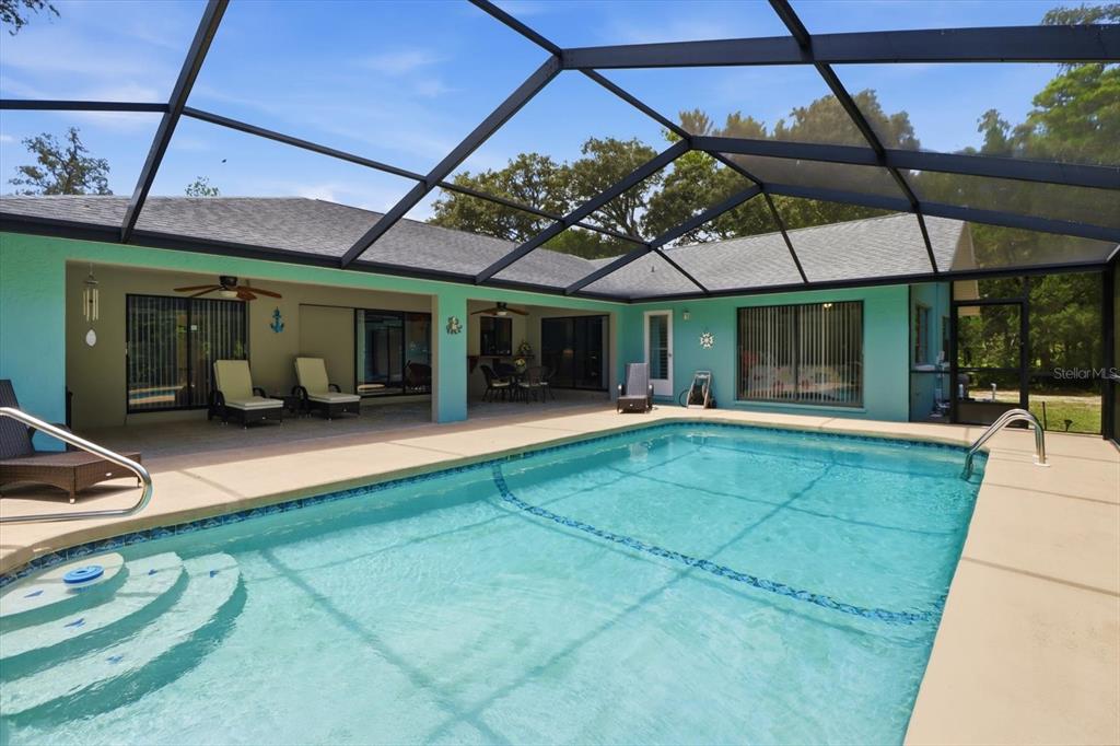 A swimming pool sits inside a screened-in lanai attached to a light blue house — 12 ASTERS COURT, HOMOSASSA, FL