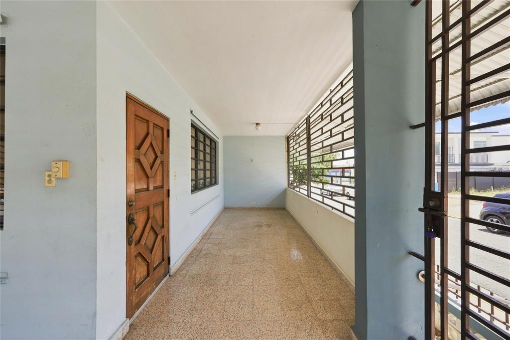 A covered porch features a wooden door, light blue walls, and a metal security gate — 16 CALLE EDUARDO QUEVEDO, ISABELA, PR