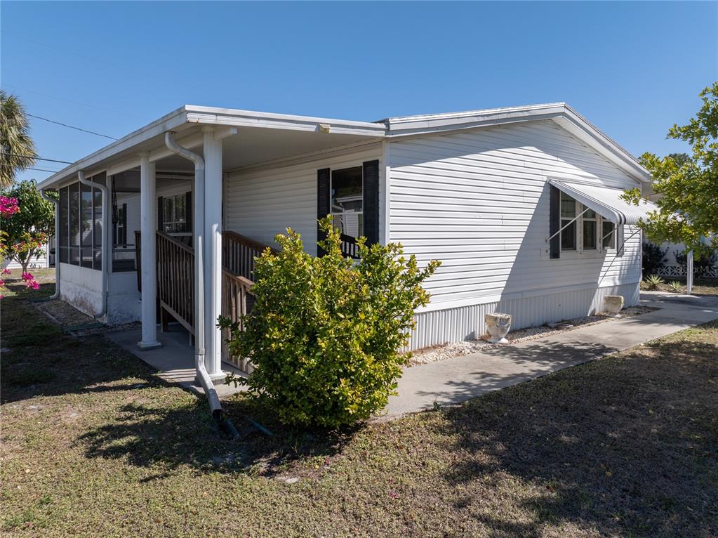 A white mobile home features a screened-in porch, a wooden ramp, and a concrete walkway — 205 CARRIAGE LANE, NORTH FORT MYERS, FL