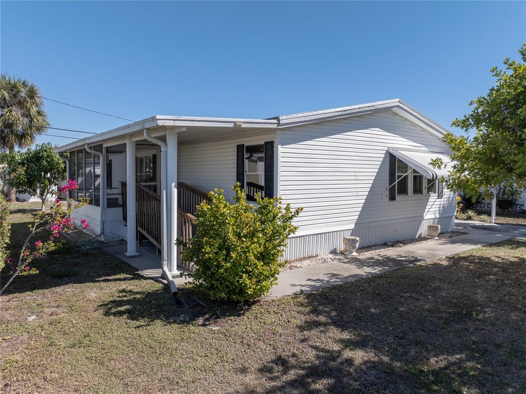 A white mobile home features a screened porch, a wooden ramp, and a concrete walkway — 205 CARRIAGE LANE, NORTH FORT MYERS, FL