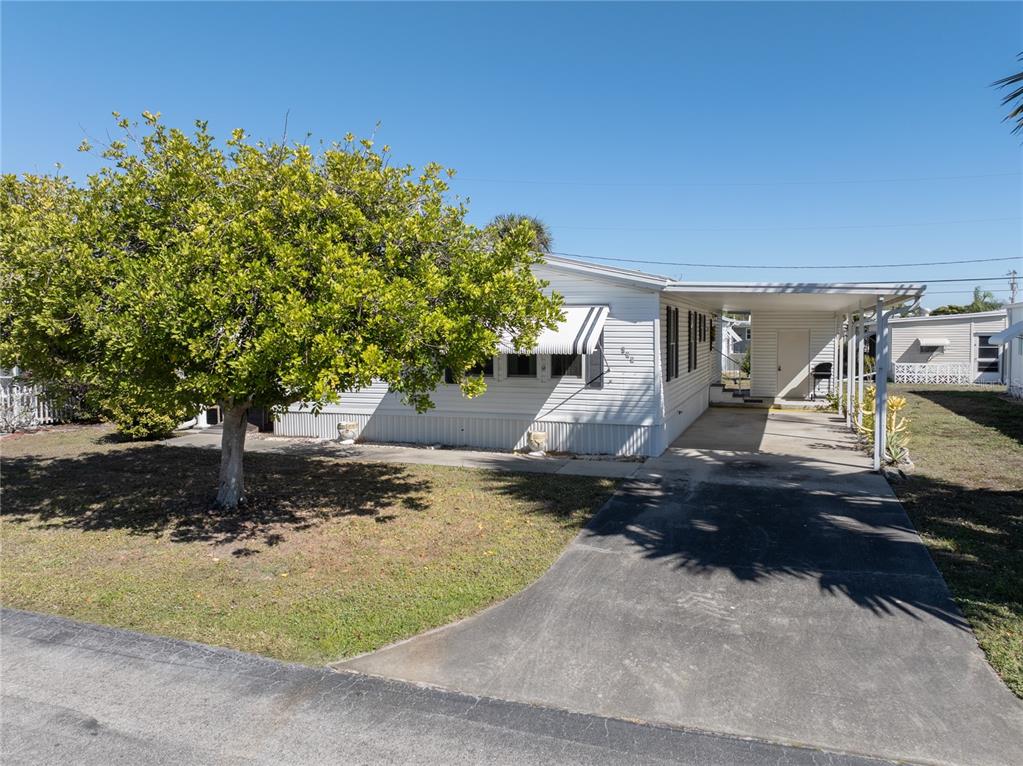 A white mobile home features a large tree in the front yard and a carport — 205 CARRIAGE LANE, NORTH FORT MYERS, FL