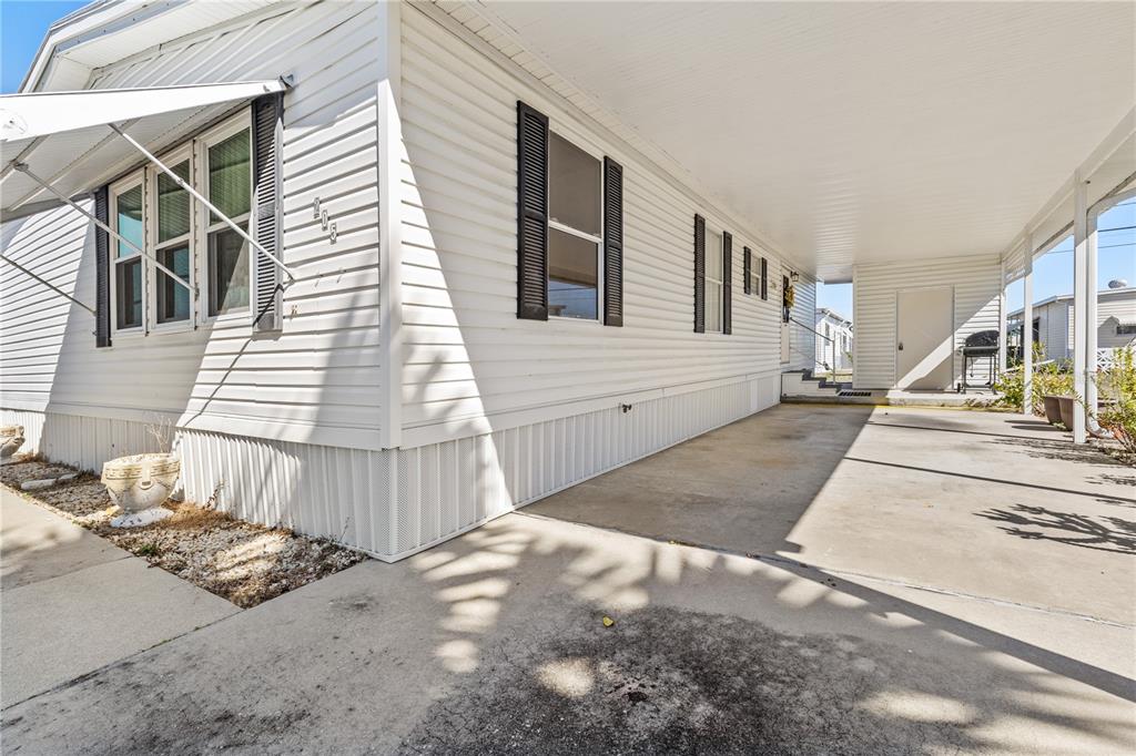 A white mobile home exterior features a concrete carport and black window shutters — 205 CARRIAGE LANE, NORTH FORT MYERS, FL