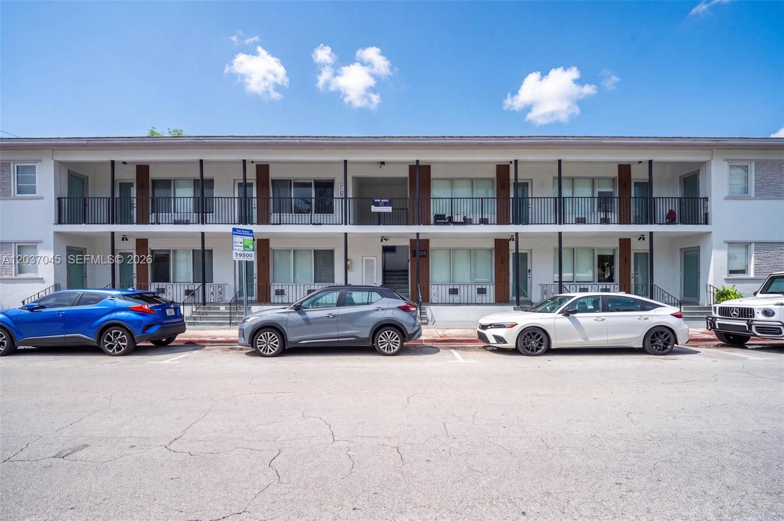 A two-story apartment building features a white exterior, black railings, and a parking lot — MIAMI BEACH, FL