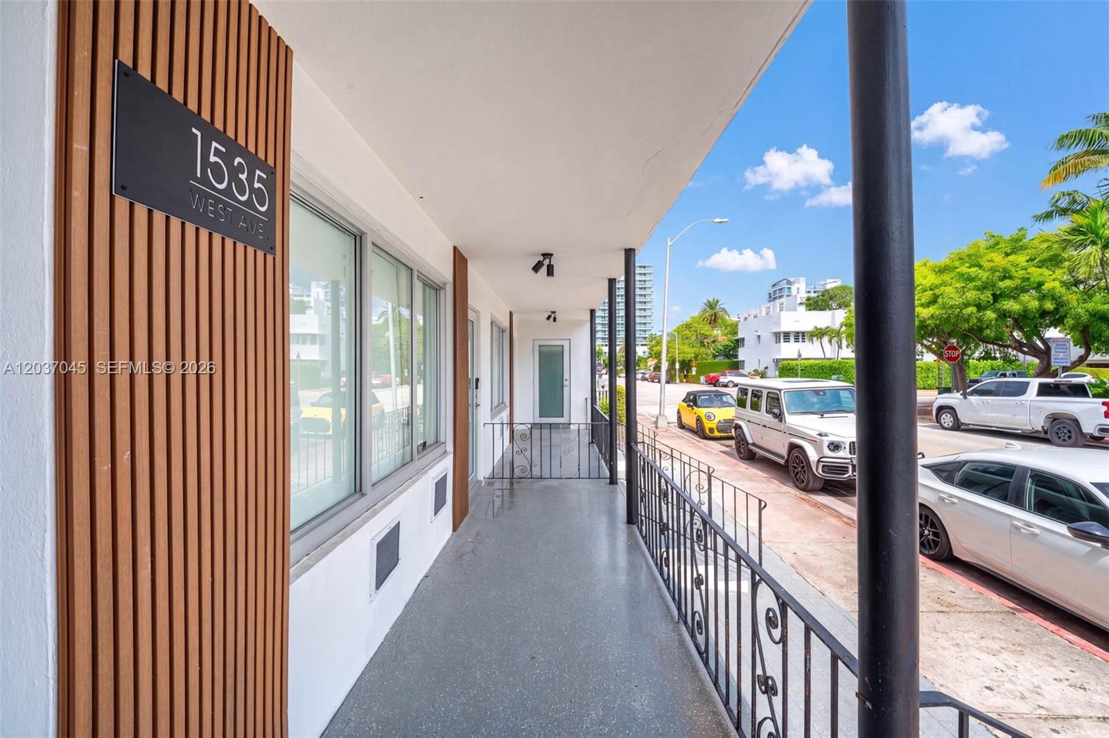 A covered outdoor walkway features a metal railing, wood-slat wall paneling, and street-side parking — MIAMI BEACH, FL